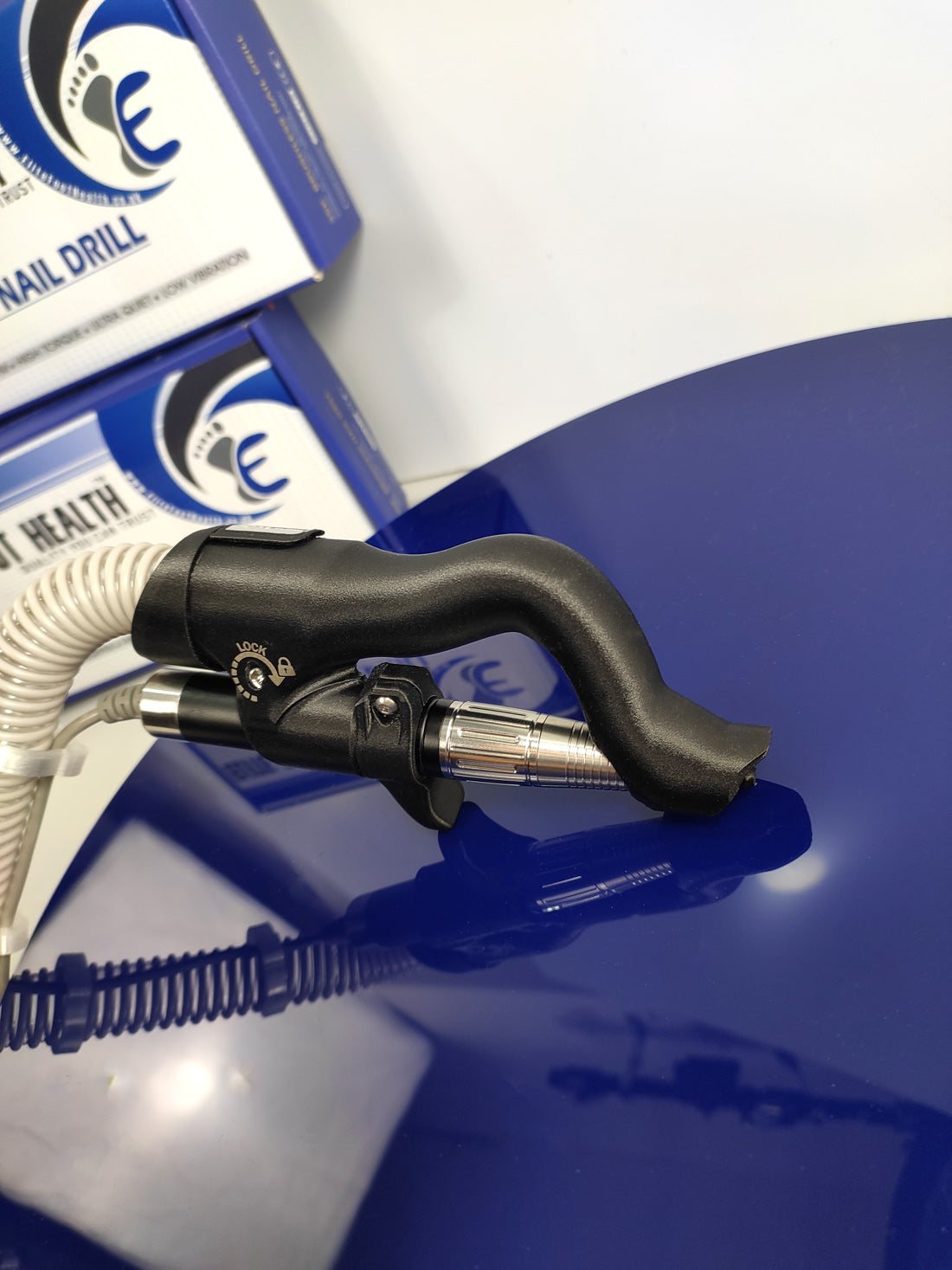 Picture shows stainless steel with black carbon-fibre infused ergonomic handpiece with extraction hose showing to left of picture, for podiatrist nail drill extraction unit, part of podiatry equipment for sale by foot care suppliers, on a blue background.