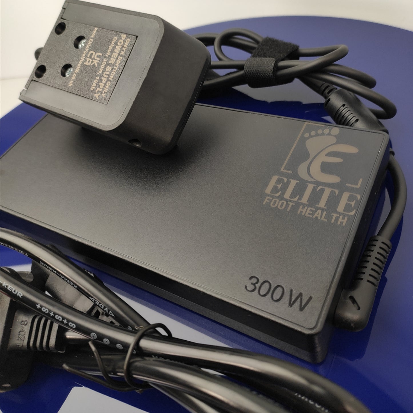Power adapter with cable on a blue surface, branded 'Elite Foot Health'.