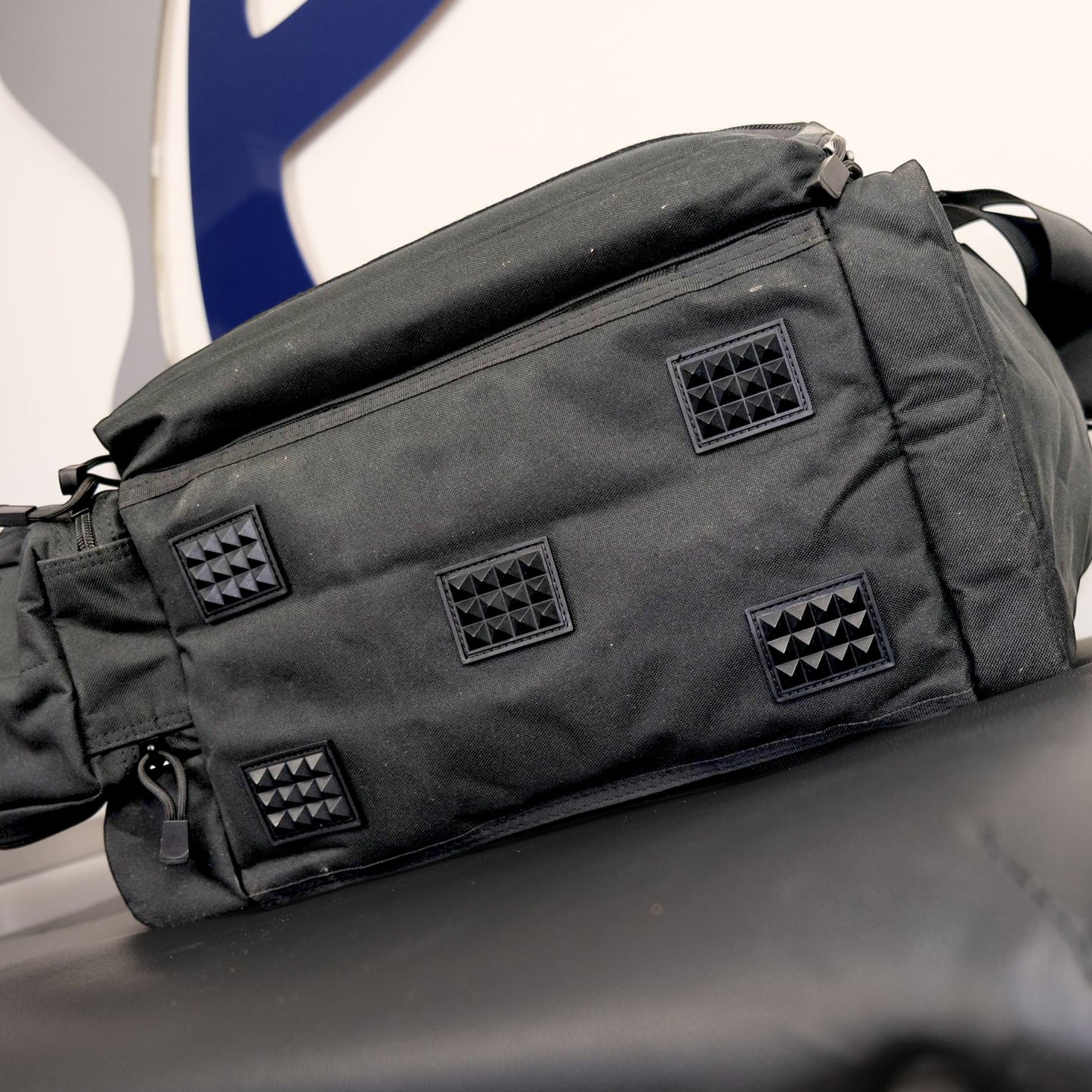 Black tactical bag with diamond pattern patches on a vehicle seat