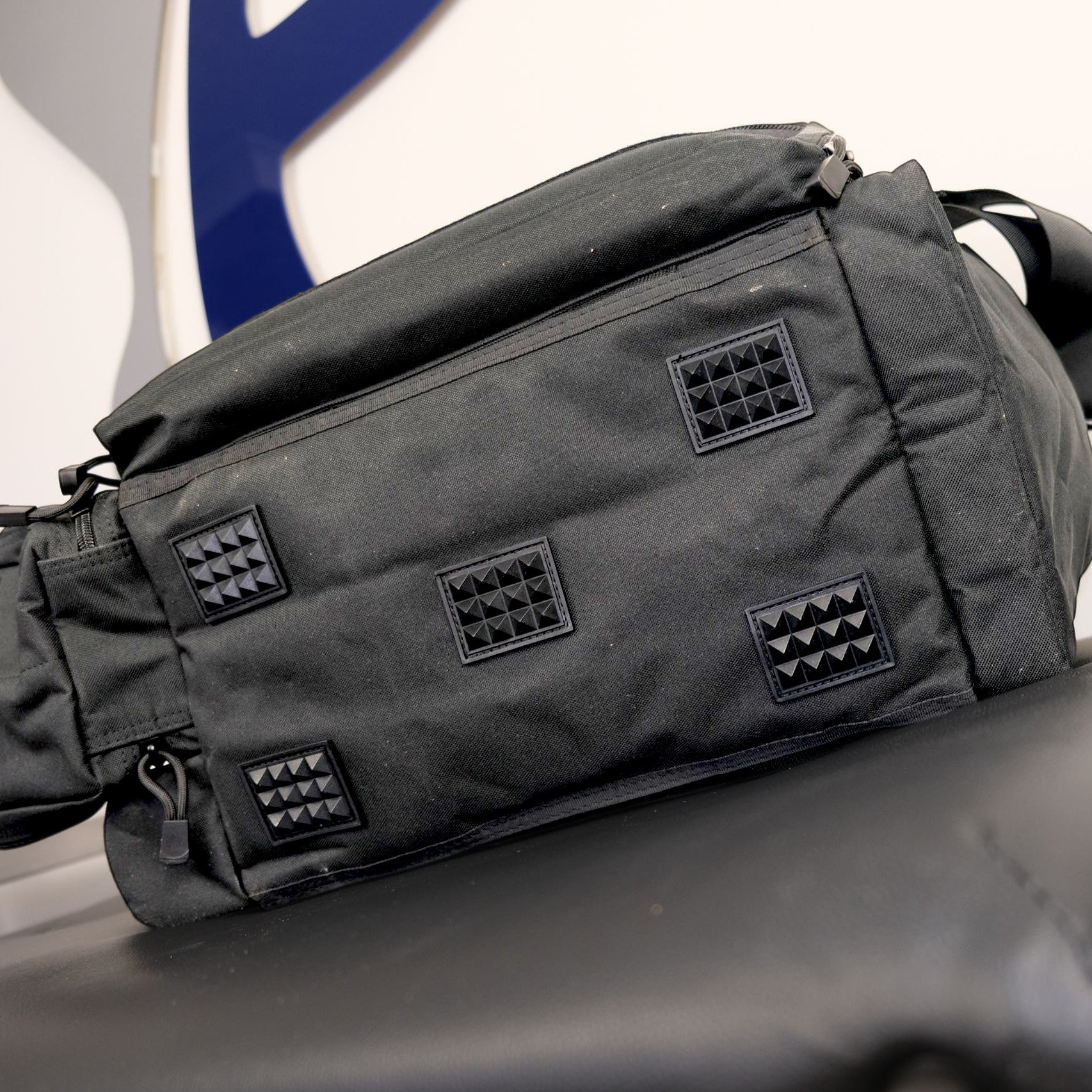 Black tactical bag with diamond pattern patches on a vehicle seat