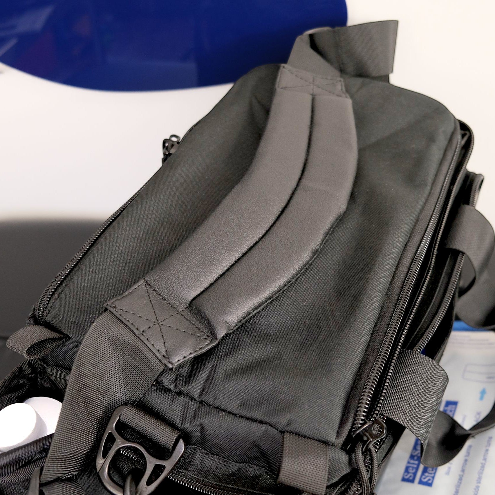 Gray backpack on a white surface with a blue object in the background
