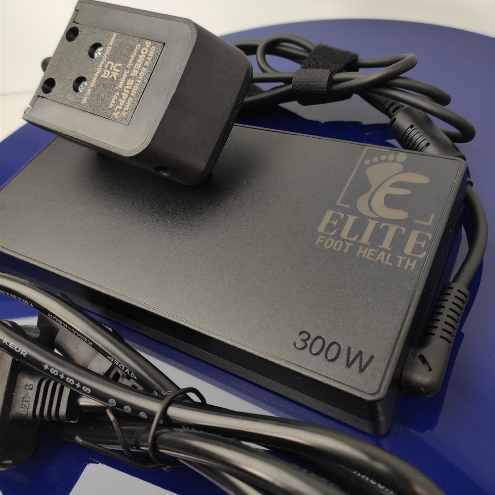 Power adapter with cable on a blue surface, branded 'Elite Foot Health'.